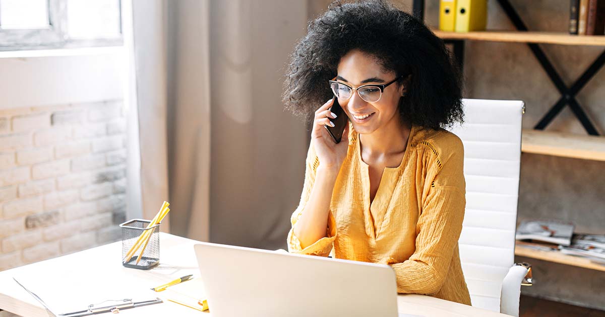 A woman working on a laptop while on the phone.