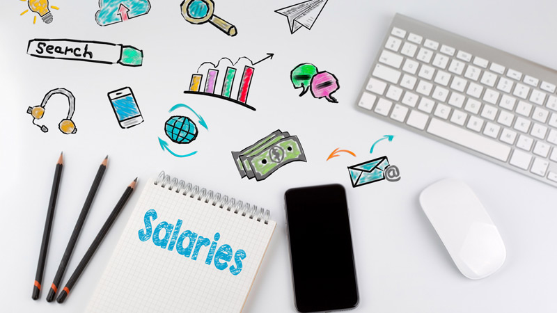 Computer keyboard, smartphone, pencils, and notepad that says Salaries next to internet-related icons.