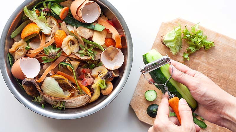Person peeling vegetables and adding the waste to a compost bowl.