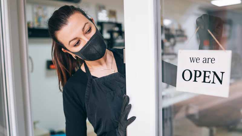 Business owner wearing a mask putting an Open sign in her shop window.
