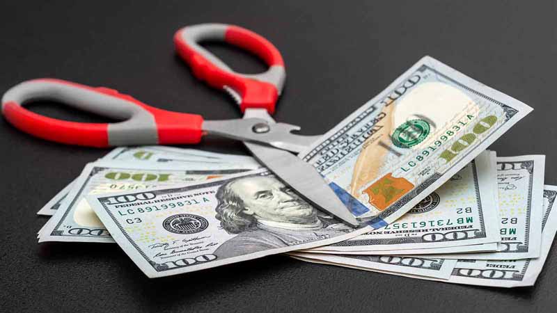 Scissors cutting money on black background.