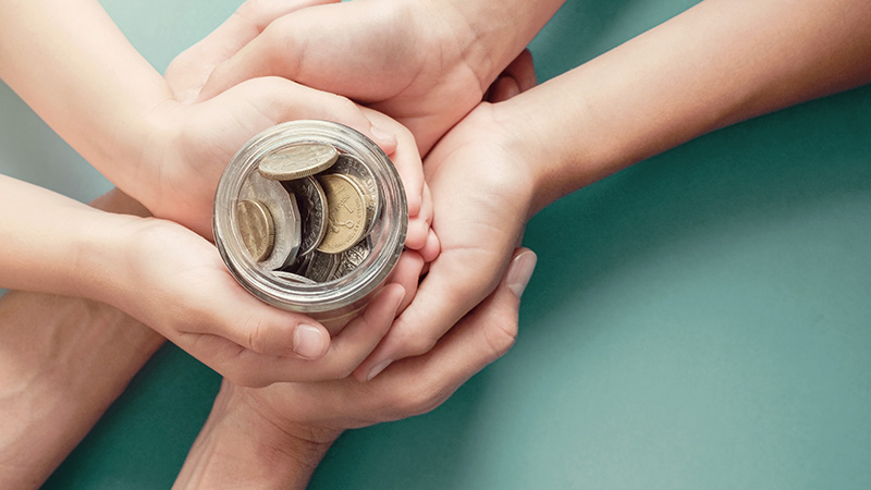 Multiple hands wrapped around a jar of coins.