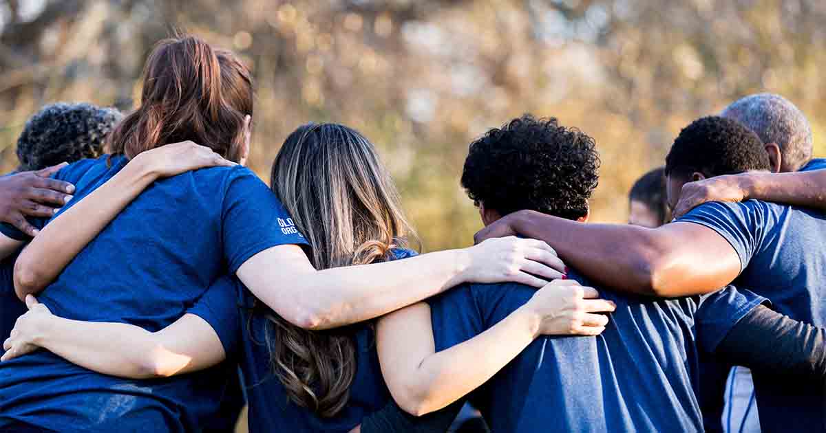 Group of friends with arms around one another in unity.
